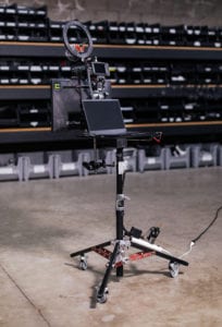 Photo of Blackmagic 6k Emmys kits in the warehouse on a stanPhoto of the Blackmagic 6k Emmys kits. On top of a stand is a monitor with a Blackmagic 6k attached to it. Attached to the Blackmagic 6k is the ring light and on-camera Rode microphone. 